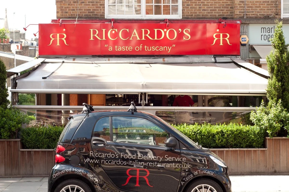 The frontage of Riccardo's on the Fulham Road, Chelsea: a red fascia sign reading Riccardo's, a taste of tuscany, above the awning and dining room window